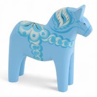 Grannas A. Olsson Hemslojd(グランナス オルソン ヘムスロイド)は、1922年にスウェーデン・ダーラナ地方ヌスナスで創業した世界最古のダラホース工房です。創業者のアンダース オルソン氏は、当初家族経営のパン屋から木工品製造へと転換し、弟らと協力してダラホースの生産を始めました。ひとつずつ選別されたスロースギ材(シルヤン湖周辺の赤松)を使い、木型の挽きから手彫り、下地塗装、さらに熟練のリップル(波模様)ペインターによるフリーハンド装飾を施します。その後、丁寧にニス仕上げされ、赤や白、青など伝統色に彩られた馬たちは、まさに「スウェーデンの象徴」として世界中の家庭や店舗に愛されています。伝統工房としての格式を受け継ぎつつも、パステルやモノトーン、限定柄などを加えることで、現代のインテリアにもマッチするデザイン性も追求しています。