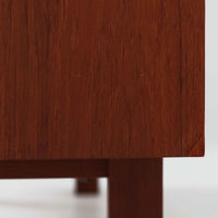 スウェーデンのBreox Moblerによるこちらのキッチンキャビネットは、温かみのあるチーク材を使用した北欧ビンテージ家具で、すっきりと直線的なフォルムと円形の木製取手が印象的な一台です。引き出し内には仕切り付きの収納も備え、カトラリーや小物の整理に便利です。扉内部は棚板付きで収納力にも優れ、中央の鍵付き扉はフラップ式でバースペースや食器収納としても活用できます。端正な佇まいと経年による木肌の深い色合いが空間に落ち着きを与える、実用性と存在感を兼ね備えた逸品です。