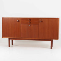 スウェーデンのBreox Moblerによるこちらのキッチンキャビネットは、温かみのあるチーク材を使用した北欧ビンテージ家具で、すっきりと直線的なフォルムと円形の木製取手が印象的な一台です。引き出し内には仕切り付きの収納も備え、カトラリーや小物の整理に便利です。扉内部は棚板付きで収納力にも優れ、中央の鍵付き扉はフラップ式でバースペースや食器収納としても活用できます。端正な佇まいと経年による木肌の深い色合いが空間に落ち着きを与える、実用性と存在感を兼ね備えた逸品です。