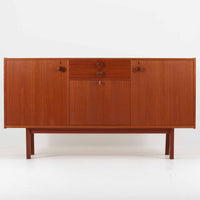 スウェーデンのBreox Moblerによるこちらのキッチンキャビネットは、温かみのあるチーク材を使用した北欧ビンテージ家具で、すっきりと直線的なフォルムと円形の木製取手が印象的な一台です。引き出し内には仕切り付きの収納も備え、カトラリーや小物の整理に便利です。扉内部は棚板付きで収納力にも優れ、中央の鍵付き扉はフラップ式でバースペースや食器収納としても活用できます。端正な佇まいと経年による木肌の深い色合いが空間に落ち着きを与える、実用性と存在感を兼ね備えた逸品です。