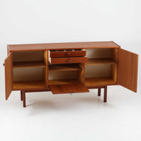 スウェーデンのBreox Moblerによるこちらのキッチンキャビネットは、温かみのあるチーク材を使用した北欧ビンテージ家具で、すっきりと直線的なフォルムと円形の木製取手が印象的な一台です。引き出し内には仕切り付きの収納も備え、カトラリーや小物の整理に便利です。扉内部は棚板付きで収納力にも優れ、中央の鍵付き扉はフラップ式でバースペースや食器収納としても活用できます。端正な佇まいと経年による木肌の深い色合いが空間に落ち着きを与える、実用性と存在感を兼ね備えた逸品です。