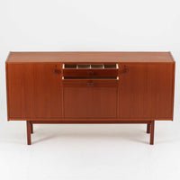 スウェーデンのBreox Moblerによるこちらのキッチンキャビネットは、温かみのあるチーク材を使用した北欧ビンテージ家具で、すっきりと直線的なフォルムと円形の木製取手が印象的な一台です。引き出し内には仕切り付きの収納も備え、カトラリーや小物の整理に便利です。扉内部は棚板付きで収納力にも優れ、中央の鍵付き扉はフラップ式でバースペースや食器収納としても活用できます。端正な佇まいと経年による木肌の深い色合いが空間に落ち着きを与える、実用性と存在感を兼ね備えた逸品です。