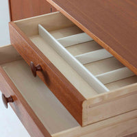 スウェーデンのBreox Moblerによるこちらのキッチンキャビネットは、温かみのあるチーク材を使用した北欧ビンテージ家具で、すっきりと直線的なフォルムと円形の木製取手が印象的な一台です。引き出し内には仕切り付きの収納も備え、カトラリーや小物の整理に便利です。扉内部は棚板付きで収納力にも優れ、中央の鍵付き扉はフラップ式でバースペースや食器収納としても活用できます。端正な佇まいと経年による木肌の深い色合いが空間に落ち着きを与える、実用性と存在感を兼ね備えた逸品です。