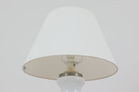 著名なデザイナー、Sidse Werner(シセ・ヴェルナー)による「BIBLIOTEK」のテーブルランプです。ペンダントランプはよく見かけますが、テーブルランプは非常に珍しいモデルです。ホルムガードならではの厚みのある高品質なガラスを使用しており、点灯するとシェードを通して柔らかな温かみのある光が広がり、空間を優雅に照らします。高さ64cmの大型サイズで存在感があり、リビングや書斎、ベッドサイドなど、あらゆるインテリアに美しく調和します。