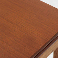 Ejner Larsen & Aksel Bender Madsenが手掛け、Naestved Mobelfabrikで製作されたエクステンションダイニングテーブルは、チーク材の天板とオーク材の脚部を組み合わせた北欧ビンテージらしい上質な佇まいが魅力です。直線的で端正なフォルムの中に、天板縁の丁寧な面取りや幕板の滑らかな造形など、当時の高い職人技が随所に感じられます。幅120cmから最大230cmまで伸長可能な構造により、日常使いから来客時まで柔軟に対応でき、空間や人数に合わせた使い方が可能です。経年変化によって深みを増した木肌の表情が、長く愛用されてきたビンテージならではの存在感を放ち、ダイニングの主役として落ち着きと品格を添えてくれる一台です。脚先には床へのダメージや汚れを防ぐためにチーク材がジョイントされており、実用性を考慮した当時の設計思想がうかがえます。また、裏面には「SKM」の刻印が確認でき、スウェーデン軍(Svenska KrigsMakten)の備品として使用されていたことを示す、背景のある希少な個体です。