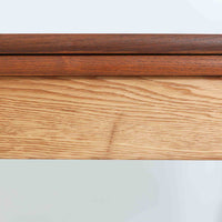 Ejner Larsen & Aksel Bender Madsenが手掛け、Naestved Mobelfabrikで製作されたエクステンションダイニングテーブルは、チーク材の天板とオーク材の脚部を組み合わせた北欧ビンテージらしい上質な佇まいが魅力です。直線的で端正なフォルムの中に、天板縁の丁寧な面取りや幕板の滑らかな造形など、当時の高い職人技が随所に感じられます。幅120cmから最大230cmまで伸長可能な構造により、日常使いから来客時まで柔軟に対応でき、空間や人数に合わせた使い方が可能です。経年変化によって深みを増した木肌の表情が、長く愛用されてきたビンテージならではの存在感を放ち、ダイニングの主役として落ち着きと品格を添えてくれる一台です。脚先には床へのダメージや汚れを防ぐためにチーク材がジョイントされており、実用性を考慮した当時の設計思想がうかがえます。また、裏面には「SKM」の刻印が確認でき、スウェーデン軍(Svenska KrigsMakten)の備品として使用されていたことを示す、背景のある希少な個体です。