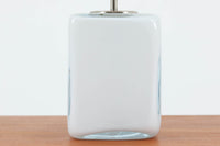 Per Lütken(ペル・ルッケン)が1980年代にデザインした「Kubus(キューブス)」シリーズのテーブルランプです。名前の通り、立方体(キューブ)をモチーフにしたホルムガードならではの厚みのある高品質なガラスが使用されており、点灯すると柔らかな光が広がり、空間に温かみと落ち着きを与えます。細いメタルの支柱が全体を引き締め、ミニマルで洗練されたデザインを際立たせています。大中小のサイズ展開がある中で、こちらは中サイズのモデルです。