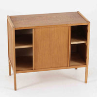 B. Fridhagenがデザインし、スウェーデンのBodafors社によって製造されたこちらのボードは、上質なオーク材を用いた小ぶりなサイズ感と、無駄を省いた洗練された意匠が魅力の一台です。スライド扉を開けると左右に仕切られた収納部が現れ、日用品や書籍の整理に最適です。細身の脚と角の立ったフレームが全体に軽やかな印象を与え、空間を圧迫せず設置できます。シンプルながらも素材の美しさと北欧らしい実用性が際立つ、希少なビンテージ家具です。