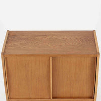 B. Fridhagenがデザインし、スウェーデンのBodafors社によって製造されたこちらのボードは、上質なオーク材を用いた小ぶりなサイズ感と、無駄を省いた洗練された意匠が魅力の一台です。スライド扉を開けると左右に仕切られた収納部が現れ、日用品や書籍の整理に最適です。細身の脚と角の立ったフレームが全体に軽やかな印象を与え、空間を圧迫せず設置できます。シンプルながらも素材の美しさと北欧らしい実用性が際立つ、希少なビンテージ家具です。