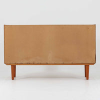 Domino Mobler社製のサイドボードは、北欧デンマークのビンテージ家具らしいシンプルかつ機能的なデザインが魅力です。チーク材を用いた温かみのある木目と深みのある色調が空間に落ち着きを与えます。左側には4杯の引き出し、右側にはスライド扉付きの収納棚を備え、食器や日用品をすっきり収めることが可能です。特徴的なスクエア型の木製ハンドルや細身の脚部が洗練された印象を与え、ダイニングやリビングでの収納家具としてだけでなく、テレビボードや飾り棚としても活躍する実用性と存在感を兼ね備えています。年月を経た風合いがより一層の魅力を引き立てる逸品です。