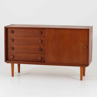 Domino Mobler社製のサイドボードは、北欧デンマークのビンテージ家具らしいシンプルかつ機能的なデザインが魅力です。チーク材を用いた温かみのある木目と深みのある色調が空間に落ち着きを与えます。左側には4杯の引き出し、右側にはスライド扉付きの収納棚を備え、食器や日用品をすっきり収めることが可能です。特徴的なスクエア型の木製ハンドルや細身の脚部が洗練された印象を与え、ダイニングやリビングでの収納家具としてだけでなく、テレビボードや飾り棚としても活躍する実用性と存在感を兼ね備えています。年月を経た風合いがより一層の魅力を引き立てる逸品です。