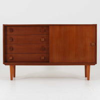 Domino Mobler社製のサイドボードは、北欧デンマークのビンテージ家具らしいシンプルかつ機能的なデザインが魅力です。チーク材を用いた温かみのある木目と深みのある色調が空間に落ち着きを与えます。左側には4杯の引き出し、右側にはスライド扉付きの収納棚を備え、食器や日用品をすっきり収めることが可能です。特徴的なスクエア型の木製ハンドルや細身の脚部が洗練された印象を与え、ダイニングやリビングでの収納家具としてだけでなく、テレビボードや飾り棚としても活躍する実用性と存在感を兼ね備えています。年月を経た風合いがより一層の魅力を引き立てる逸品です。