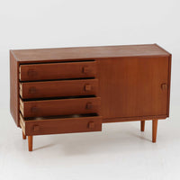 Domino Mobler社製のサイドボードは、北欧デンマークのビンテージ家具らしいシンプルかつ機能的なデザインが魅力です。チーク材を用いた温かみのある木目と深みのある色調が空間に落ち着きを与えます。左側には4杯の引き出し、右側にはスライド扉付きの収納棚を備え、食器や日用品をすっきり収めることが可能です。特徴的なスクエア型の木製ハンドルや細身の脚部が洗練された印象を与え、ダイニングやリビングでの収納家具としてだけでなく、テレビボードや飾り棚としても活躍する実用性と存在感を兼ね備えています。年月を経た風合いがより一層の魅力を引き立てる逸品です。