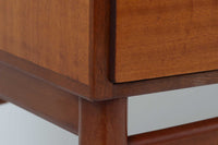 FDBモブラーでBorge mogensenの後任としてアートディレクターを務めたPoul m. Voltherによる、美しく洗練されたキャビネット。良質なマホガニー材の本体に、ビーチ材の脚部を組み合わせたコントラストが魅力です。真鍮の丸い鍵穴が特徴的な3枚の扉を備え、中央には調節可能な棚、両側には精巧な蟻継ぎが施された移動式の引き出しを配しています。下部には真鍮の俵型ハンドル付きの引き出しが3杯並び、細部へのこだわりが際立ちます。また、室内で靴を履く文化に配慮し、脚先には汚れ防止のための濃い塗装が施されています。1950年代にデザインされた本作は、先細りの脚やストレッチャーがミニマルな美しさを際立たせる一方、シンメトリーなフォルムや真鍮の装飾が伝統的なエレガンスを醸し出し、モダンとクラシックが調和した逸品です。