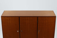 FDBモブラーでBorge mogensenの後任としてアートディレクターを務めたPoul m. Voltherによる、美しく洗練されたキャビネット。良質なマホガニー材の本体に、ビーチ材の脚部を組み合わせたコントラストが魅力です。真鍮の丸い鍵穴が特徴的な3枚の扉を備え、中央には調節可能な棚、両側には精巧な蟻継ぎが施された移動式の引き出しを配しています。下部には真鍮の俵型ハンドル付きの引き出しが3杯並び、細部へのこだわりが際立ちます。また、室内で靴を履く文化に配慮し、脚先には汚れ防止のための濃い塗装が施されています。1950年代にデザインされた本作は、先細りの脚やストレッチャーがミニマルな美しさを際立たせる一方、シンメトリーなフォルムや真鍮の装飾が伝統的なエレガンスを醸し出し、モダンとクラシックが調和した逸品です。