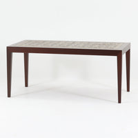 Nils Thorssonがデザインを手掛け、Royal CopenhagenのBACAシリーズのタイルを天板に配したセンターテーブルです。家具メーカーHaslev社により製作され、マホガニー材の落ち着いた木目と、幾何学的で温かみのあるタイル意匠が美しく調和しています。直線的で端正なフォルムは空間をすっきりと見せ、リビングの主役としてはもちろん、ソファ前のローテーブルとしても活躍。経年により深みを増した木部と味わい豊かな陶板が、北欧ビンテージならではの存在感を放つ一品です。