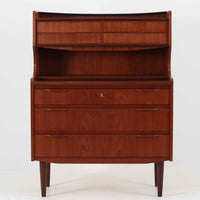 デンマーク製のチーク材によるライティングビューロです。幅85cmと程よいサイズ感で、上段には小引き出しを備え、小物や文具を整理しやすい構造になっています。中央のライティング天板は手前にスライドさせることで作業スペースが確保でき、書き物やノートPCの使用に最適です。さらに、内部には鏡が備わっており、ドレッサーとしても活用できる実用的なデザインです。下段には容量の大きな引き出しが3杯あり、衣類や書類の収納にも対応します。チーク材特有の温かみのある木目と経年による艶が味わい深く、実用性と美観を兼ね備えたビンテージ家具です。