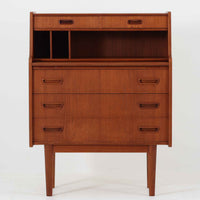 デンマーク製のビンテージライティングビューロは、上部に引き出しと仕切り棚、下部に3段のチェストを備えた実用的な設計が魅力です。チーク材の美しい木目と丸みを帯びた側面のフレームが柔らかな印象を与え、天板を引き出すことで書き物スペースとしても活用可能。コンパクトながらも多機能で、リビングや寝室での整理整頓に役立つ一台です。