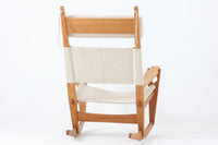 Hans J. Wegnerが1967年にデザインしたロッキングチェア「キーホールチェア(GE673)」は、GETAmA社製の一脚です。特徴的な「鍵穴」のような形状の座面固定方法が名前の由来で、左右のアーム下に引っ掛けた2本の棒が座面を支える構造です。帆布製の背もたれと座面は、ハンモックのような座り心地を提供し、まるで包み込まれるような安心感を感じさせます。ロッキングチェアならではの揺れと、程よい可動領域が特徴で、家の中でゆったりとくつろぐのに最適です。座面は簡単に取り外せ、クリーニングにも配慮されています。軽量で機能性とデザインが見事に調和した、ウェグナーならではの作品です。