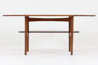 台形を基にした多角形の天板が特徴的な、美しいビンテージのセンターテーブル。心地よい木目が際立つウォールナット材の天板と、ナチュラルな風合いのビーチ材の組み合わせが、温かみのある佇まいを演出しています。天板と脚部、棚板の接続部には丸い真鍮があしらわれ、シンプルなフォルムの中に洗練されたアクセントを加えています。また、脚部をつなぐ幕板の形状も独特で、細部にまでこだわりが感じられるデザインです。デザイナーは不明ですが、細部の仕上げや素材選びから高いクオリティがうかがえる一品。モダンとクラシックが絶妙に調和した、上質なビンテージテーブルです。