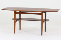 台形を基にした多角形の天板が特徴的な、美しいビンテージのセンターテーブル。心地よい木目が際立つウォールナット材の天板と、ナチュラルな風合いのビーチ材の組み合わせが、温かみのある佇まいを演出しています。天板と脚部、棚板の接続部には丸い真鍮があしらわれ、シンプルなフォルムの中に洗練されたアクセントを加えています。また、脚部をつなぐ幕板の形状も独特で、細部にまでこだわりが感じられるデザインです。デザイナーは不明ですが、細部の仕上げや素材選びから高いクオリティがうかがえる一品。モダンとクラシックが絶妙に調和した、上質なビンテージテーブルです。