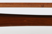 台形を基にした多角形の天板が特徴的な、美しいビンテージのセンターテーブル。心地よい木目が際立つウォールナット材の天板と、ナチュラルな風合いのビーチ材の組み合わせが、温かみのある佇まいを演出しています。天板と脚部、棚板の接続部には丸い真鍮があしらわれ、シンプルなフォルムの中に洗練されたアクセントを加えています。また、脚部をつなぐ幕板の形状も独特で、細部にまでこだわりが感じられるデザインです。デザイナーは不明ですが、細部の仕上げや素材選びから高いクオリティがうかがえる一品。モダンとクラシックが絶妙に調和した、上質なビンテージテーブルです。