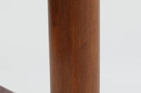 台形を基にした多角形の天板が特徴的な、美しいビンテージのセンターテーブル。心地よい木目が際立つウォールナット材の天板と、ナチュラルな風合いのビーチ材の組み合わせが、温かみのある佇まいを演出しています。天板と脚部、棚板の接続部には丸い真鍮があしらわれ、シンプルなフォルムの中に洗練されたアクセントを加えています。また、脚部をつなぐ幕板の形状も独特で、細部にまでこだわりが感じられるデザインです。デザイナーは不明ですが、細部の仕上げや素材選びから高いクオリティがうかがえる一品。モダンとクラシックが絶妙に調和した、上質なビンテージテーブルです。