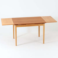 チーク材とビーチ材を組み合わせたデンマーク製のエクステンションダイニングテーブル。天板には深みのあるチーク材、脚部、幕板、拡張板には明るいビーチ材を使用し、異素材のコントラストが洗練された印象を与えます。幅100cmとコンパクトながら、両側に伸長式リーフを備え、用途に応じて天板の拡張が可能。シンプルで堅牢なつくりは、限られた空間にもフィットし、経年変化による木材の味わいとともに、長く愛用できる北欧ビンテージ家具の魅力が詰まった一台です。