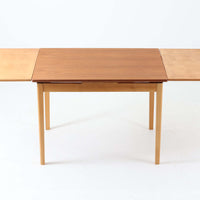 チーク材とビーチ材を組み合わせたデンマーク製のエクステンションダイニングテーブル。天板には深みのあるチーク材、脚部、幕板、拡張板には明るいビーチ材を使用し、異素材のコントラストが洗練された印象を与えます。幅100cmとコンパクトながら、両側に伸長式リーフを備え、用途に応じて天板の拡張が可能。シンプルで堅牢なつくりは、限られた空間にもフィットし、経年変化による木材の味わいとともに、長く愛用できる北欧ビンテージ家具の魅力が詰まった一台です。