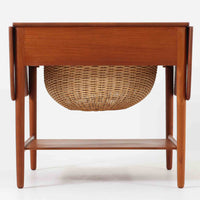 Hans J. Wegnerがデザインし、Andreas Tuck社から発表されたAT33ソーイングテーブルは、チーク無垢材を贅沢に用いた希少なモデルです。両側のバタフライ式天板で作業スペースを拡張でき、仕切り付きの引き出しとラタン製バスケットが裁縫道具や小物を美しく収納します。下段の棚板も備えた実用性の高い構造で、繊細な造作と職人技が光る北欧ビンテージ家具の逸品です。