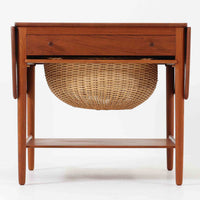 Hans J. Wegnerがデザインし、Andreas Tuck社から発表されたAT33ソーイングテーブルは、チーク無垢材を贅沢に用いた希少なモデルです。両側のバタフライ式天板で作業スペースを拡張でき、仕切り付きの引き出しとラタン製バスケットが裁縫道具や小物を美しく収納します。下段の棚板も備えた実用性の高い構造で、繊細な造作と職人技が光る北欧ビンテージ家具の逸品です。