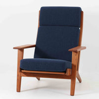 Hans J. Wegnerがデザインし、Getama社によって製造されたGe290Aは、現在では希少となったチーク材のフレームに深いブルーの張地が美しく調和した、ハイバック仕様のビンテージシングルソファです。緩やかに傾斜する背もたれと幅広のアームが身体を包み込むような快適な座り心地を実現し、日常に上質な寛ぎをもたらします。背面の格子状フレームや真鍮ビスなど、細部にまでウェグナーの美意識が宿り、北欧家具の名作としてリビングの主役にふさわしい存在感を放ちます。座面クッションにはスプリングが内包されていますが、背もたれにはウレタンのみが使用されています。