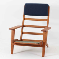 Hans J. Wegnerがデザインし、Getama社によって製造されたGe290Aは、現在では希少となったチーク材のフレームに深いブルーの張地が美しく調和した、ハイバック仕様のビンテージシングルソファです。緩やかに傾斜する背もたれと幅広のアームが身体を包み込むような快適な座り心地を実現し、日常に上質な寛ぎをもたらします。背面の格子状フレームや真鍮ビスなど、細部にまでウェグナーの美意識が宿り、北欧家具の名作としてリビングの主役にふさわしい存在感を放ちます。座面クッションにはスプリングが内包されていますが、背もたれにはウレタンのみが使用されています。