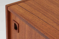 温かみのある木目が美しいチーク材を使用した、北欧ビンテージの小ぶりなローボードです。幅88cmとコンパクトながら、存在感のある佇まいで空間に上品なアクセントを加えます。引き戸の丸みを帯びた掘り込み取っ手や先細りの脚部など、シンプルながらも細部にまでこだわった北欧らしいデザインが魅力です。収納部には棚板が設けられていた形跡がありますが、現在は欠品しております。お気に入りの本や雑貨を飾るディスプレイ用としてもお楽しみいただけます。テレビ台やエントランスの収納など、多用途に活躍してくれる一台です。