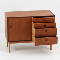 デンマーク製の小ぶりな北欧ビンテージボードで、チーク材とオーク材の組み合わせが上品な一台です。幅90cmとコンパクトながら、引き出し4杯とスライド扉付きの収納部を備え、実用性に優れています。丸いくり抜きの取っ手や直線的な脚部のデザインが軽快な印象を与え、どんな空間にも馴染みやすい造りです。背面の収納部には配線用の穴があり、オーディオや小型テレビ台としても活用可能です。経年により深みを増した木肌が、北欧家具ならではの味わいを感じさせます。