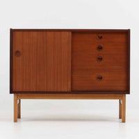デンマーク製の小ぶりな北欧ビンテージボードで、チーク材とオーク材の組み合わせが上品な一台です。幅90cmとコンパクトながら、引き出し4杯とスライド扉付きの収納部を備え、実用性に優れています。丸いくり抜きの取っ手や直線的な脚部のデザインが軽快な印象を与え、どんな空間にも馴染みやすい造りです。背面の収納部には配線用の穴があり、オーディオや小型テレビ台としても活用可能です。経年により深みを増した木肌が、北欧家具ならではの味わいを感じさせます。