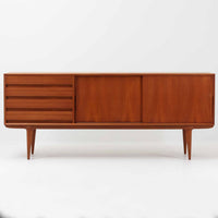 Gunni Omannがデザインし、Omann Jun社によって製造されたModel 18は、洗練されたラインと実用性を兼ね備えた北欧ビンテージの名作サイドボードです。チーク材の美しい木目が前面に広がり、引き出しとスライド扉の組み合わせが高い収納力を実現しています。特に繊細に削り出された取手や先細りの脚部が、軽やかで彫刻的な印象を与え、空間を上質に演出します。幅200cmのサイズ感は、リビングやダイニングの主役として活躍する存在感ある一台です。
