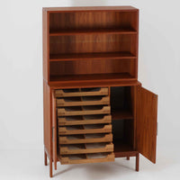 Bjerringbro Savvaerkによるチーク材キャビネットは、上下に分かれた構成と可動棚を備えた収納力の高さが魅力です。上段は3段のシェルフ、下段は珍しいポケットドア構造の扉内にA4サイズの書類が収納可能な引き出し型トレイが8段並び、書類や小物の整理に適しています。直線的で端正なフォルムと、チーク材の木目が美しく調和した佇まいは、北欧ビンテージらしい実用性と美しさを兼ね備えた逸品です。