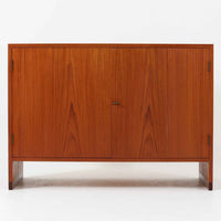 Hans J. Wegner(ハンス・J・ウェグナー)によってデザインされ、RY Mobler社により製造されたこちらのキャビネットは、美しいチーク材と実用的な構造が融合した北欧ビンテージ家具の名作です。扉にはチーク材特有の深い木目が活かされ、中央の控えめな金属製ハンドルがアクセントとなっています。内部は可動棚付きの2室構成で、食器類や書類、小物の整理にも適した収納力を備えています。注目すべきは、足摺にあたる下部のパーツにオーク材が使用されている点で、異なる木材の組み合わせが上質なコントラストを生み出しています。背面には「RY」ロゴと「27 APR 1959」のスタンプが残っており、当時のオリジナルであることが確認できます。リビングやダイニング、書斎などさまざまな空間で、温もりと凛とした佇まいを演出してくれる北欧ビンテージ家具らしい一台です。