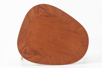 Holger Georg Jensen(ホルガー・ジョージ・イェンセン)によってデザインされ、Kubus moblerから製造されたデンマーク製ビンテージのサイドテーブルです。有機的な曲線を描く天板と、それを支える3本脚の構造が美しいバランスを保っています。天板下には同形状の棚板が設けられており、雑誌や小物の収納にも便利です。素材には艶やかなチーク材が用いられ、天板の木目の美しさも際立っています。北欧モダンを感じさせる上品な佇まいで、ソファサイドやベッドサイドにおすすめの一台です。