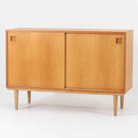 オーク材の美しい木目と柔らかな色味が魅力のこちらのボードは、幅120cmと使い勝手の良いサイズ感で、北欧ビンテージらしい洗練された佇まいが魅力です。内部には可動棚とフェルト付きの浅型引き出しが備えられ、日用品や小物の整理に最適。彫り込み式の取手やテーパードレッグなど、細部にまで配慮された上質な造りが光ります。販売店ラベルとして「Nr. Uttrup Boligmontering」が残されており、当時の流通背景を感じさせる一点物のアイテムです。