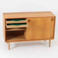 オーク材の美しい木目と柔らかな色味が魅力のこちらのボードは、幅120cmと使い勝手の良いサイズ感で、北欧ビンテージらしい洗練された佇まいが魅力です。内部には可動棚とフェルト付きの浅型引き出しが備えられ、日用品や小物の整理に最適。彫り込み式の取手やテーパードレッグなど、細部にまで配慮された上質な造りが光ります。販売店ラベルとして「Nr. Uttrup Boligmontering」が残されており、当時の流通背景を感じさせる一点物のアイテムです。