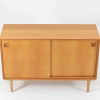 オーク材の美しい木目と柔らかな色味が魅力のこちらのボードは、幅120cmと使い勝手の良いサイズ感で、北欧ビンテージらしい洗練された佇まいが魅力です。内部には可動棚とフェルト付きの浅型引き出しが備えられ、日用品や小物の整理に最適。彫り込み式の取手やテーパードレッグなど、細部にまで配慮された上質な造りが光ります。販売店ラベルとして「Nr. Uttrup Boligmontering」が残されており、当時の流通背景を感じさせる一点物のアイテムです。