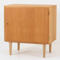 Poul Hundevadがデザインし、Hundevad & Co社から製造されたこちらのキャビネットは、上質なオーク材を用いた小ぶりな北欧ビンテージ品で、すっきりとした面構えと繊細な脚部が印象的な一台です。鍵付きの開き戸を備え、内部には棚板が設けられており、収納家具としての実用性に加え、空間にナチュラルで落ち着いた佇まいをもたらします。なお、脚部は後年に交換されている可能性がありますが、全体の雰囲気を損なわない自然な仕上がりです。