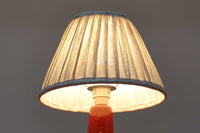 デンマークの照明ブランドLe Klint(レ・クリント)のテーブルランプで、デザイナーはOle Boggild(オーレ・ボギル)。艶やかなレッドの釉薬が美しく、ふっくらと丸みを帯びたフォルムが愛らしくも上品な印象を与えます。シェードはLe Klint社製ではありませんが、新品のリネン製プリーツシェードを合わせており、クラシカルな佇まいと柔らかな光を演出します。北欧らしい温かみと洗練された存在感を持ち、ベッドサイドやリビングのアクセントとして取り入れやすい一灯です。