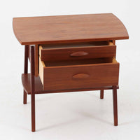 チーク材を用いたこちらの2段チェストは、緩やかにカーブした天板と舟形の引き手が特徴的な北欧ビンテージ家具です。幅64cmとコンパクトながらも引き出し2杯と下部の棚板を備え、収納力とディスプレイ性を兼ね備えています。テーパー脚が軽やかな印象を与え、ベッドサイドやリビングのサイドテーブルとしても活躍。年月を経た木肌の温かみが、空間に落ち着きと味わい深い存在感をもたらす一品です。