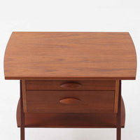 チーク材を用いたこちらの2段チェストは、緩やかにカーブした天板と舟形の引き手が特徴的な北欧ビンテージ家具です。幅64cmとコンパクトながらも引き出し2杯と下部の棚板を備え、収納力とディスプレイ性を兼ね備えています。テーパー脚が軽やかな印象を与え、ベッドサイドやリビングのサイドテーブルとしても活躍。年月を経た木肌の温かみが、空間に落ち着きと味わい深い存在感をもたらす一品です。