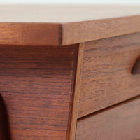 チーク材を用いたこちらの2段チェストは、緩やかにカーブした天板と舟形の引き手が特徴的な北欧ビンテージ家具です。幅64cmとコンパクトながらも引き出し2杯と下部の棚板を備え、収納力とディスプレイ性を兼ね備えています。テーパー脚が軽やかな印象を与え、ベッドサイドやリビングのサイドテーブルとしても活躍。年月を経た木肌の温かみが、空間に落ち着きと味わい深い存在感をもたらす一品です。