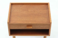 デンマークを代表する家具デザイナー、Hans J. Wegner(ハンス・J・ウェグナー)によってデザインされた、Ry mobler社製のビンテージサイドテーブルです。素材にはあたたかみのあるオーク材が使用されており、北欧らしいシンプルで機能的な美しさが感じられます。天板には縁に立ち上がりが設けられており、小物が転がり落ちにくい実用的な仕様。引き出しとオープンスペースが組み合わされたデザインで、ベッドサイドやソファ横、玄関周りなど様々なシーンで活躍します。無駄のないフォルムと丸脚の柔らかな佇まいが魅力で、ウェグナーデザインならではの美しいバランスが光る一台です。背板には、同モデルとしては珍しくオーク材ではなくmDFと思われる素材が使用されています。また、天板には目立つ傷がございますため、その点を考慮した価格設定とさせていただいております。
