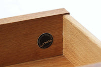 デンマークを代表する家具デザイナー、Hans J. Wegner(ハンス・J・ウェグナー)によってデザインされた、Ry mobler社製のビンテージサイドテーブルです。素材にはあたたかみのあるオーク材が使用されており、北欧らしいシンプルで機能的な美しさが感じられます。天板には縁に立ち上がりが設けられており、小物が転がり落ちにくい実用的な仕様。引き出しとオープンスペースが組み合わされたデザインで、ベッドサイドやソファ横、玄関周りなど様々なシーンで活躍します。無駄のないフォルムと丸脚の柔らかな佇まいが魅力で、ウェグナーデザインならではの美しいバランスが光る一台です。背板には、同モデルとしては珍しくオーク材ではなくmDFと思われる素材が使用されています。また、天板には目立つ傷がございますため、その点を考慮した価格設定とさせていただいております。